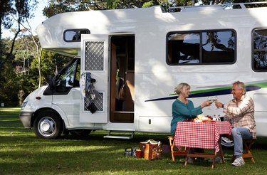 Mature couple having picnic by motor home in park, toasting
