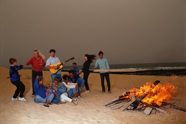 Group of people dancing around fire, man playing guitar