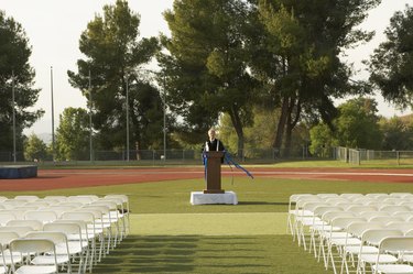 Lecturer standing at podium in front of empty seats outdoors