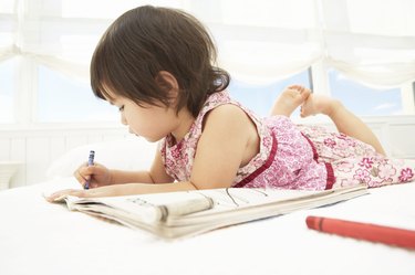 Toddler girl (21-24 months) coloring on bed, side view