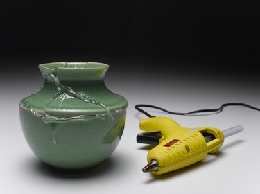 Broken green vase glued together beside yellow glue gun