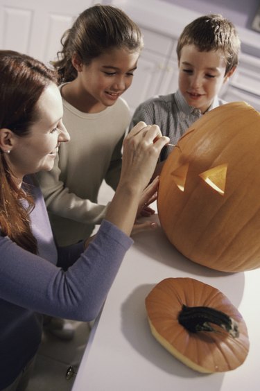 Mother carving a pumpkin with her son and daughter