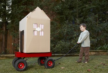 Boy (6-7) transporting cardboard house on cart