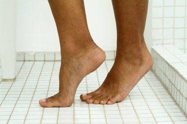 Image of person's feet standing on tiptoes on tile floor in bathroom, close-up