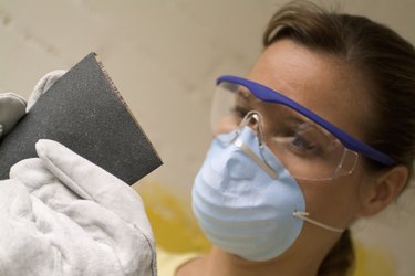 Close-up of a woman holding sand paper wearing a dust mask and safety goggles