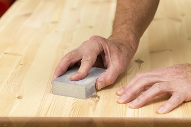 Mans hand on sanding block with pine wood