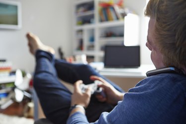 Teenage Boy Playing Video Game And Talking On Mobile Phone