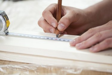 Male hands using measuring tape on wooden board