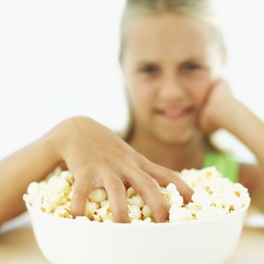 Portrait of a young girl (11-12) with her hand in a bowl of popcorn
