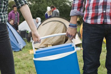 People carrying cooler by campsite