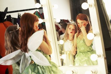 Two girls (5-8) in costumes looking at reflections in backstage mirror