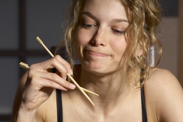 Young woman holding chopsticks, smiling