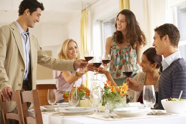 Group of young people raising glasses at dinner table, smiling
