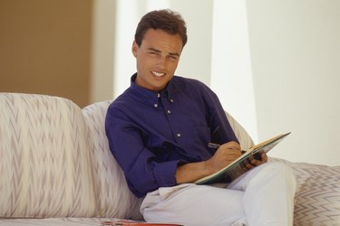 Young man sitting on couch, writing, portrait