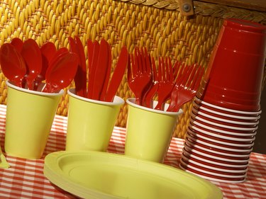Plastic utensils, cups, and plates sitting next to a picnic basket