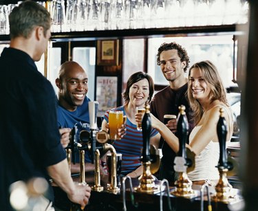 Four Friends Toasting Drinks in a Pub while a Barman Fills a Glass