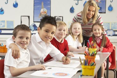 Group Of Primary Schoolchildren And Teacher Working At Desks In Classroom