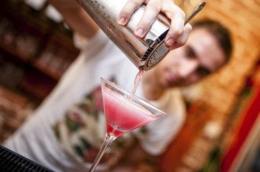 barman preparing and pouring cosmopolitan alcoholic cocktail drink