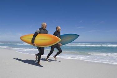 Surfers running on beach in wetsuits