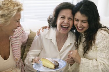Three women laughing, one holding peice of cake