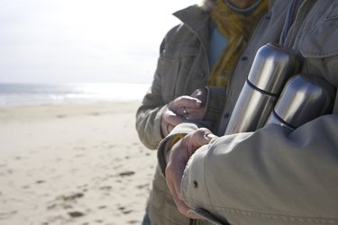 Couple with insulated flasks on beach, mid section