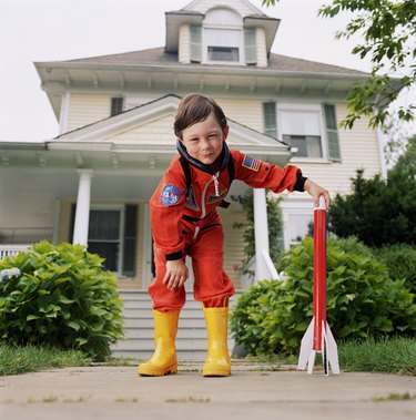 Boy (3-5) in yellow wellington boots, hand on toy rocket, portrait