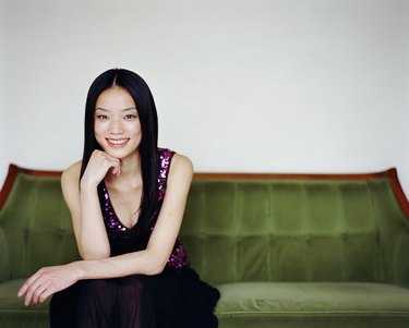 Young woman sitting on sofa, resting chin on hand, smiling