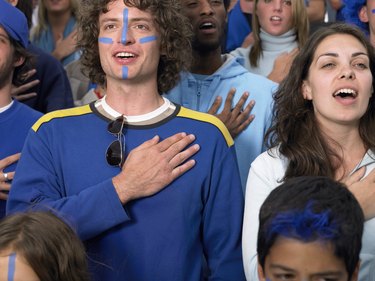 Stadium crowd, fans singing with hands held over heart, close-up