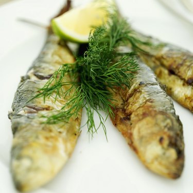 Close-up of whole fried fish garnished with chives and a lemon half