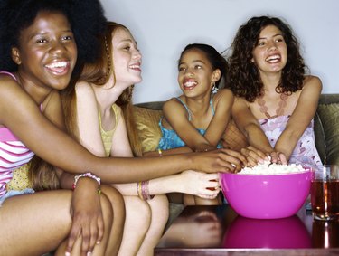 Close-up of four teenage girls sitting smiling at table with popcorn