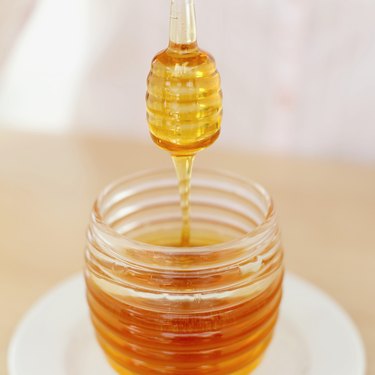 close-up of a honey dipper over a jar of honey