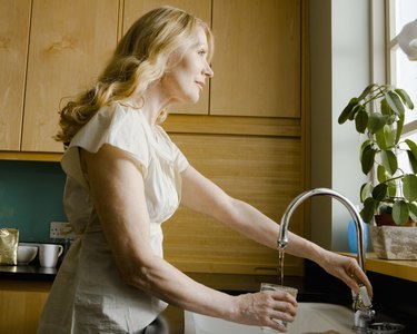 Woman pouring glass of water from faucet