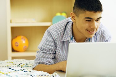 Teenage boy (13-14) lying on bed, using laptop