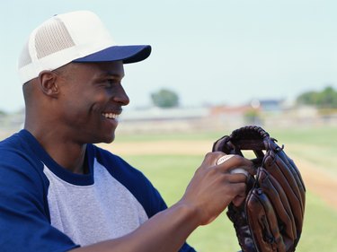 Baseball player holding baseball glove with ball, smiling, side view