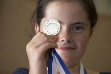 Girl (9-11) holding sports medal in front of eye