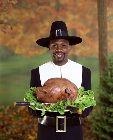 Man in pilgrim costume holding roasted turkey