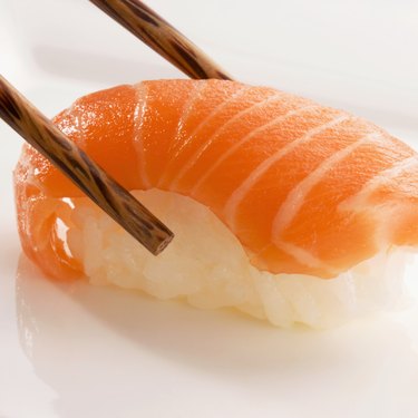 Close-up of Nigiri sushi with salmon held between chopsticks