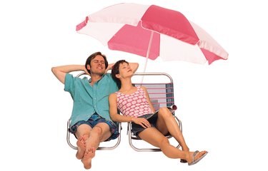 Couple reclining on lounge chairs under beach umbrella