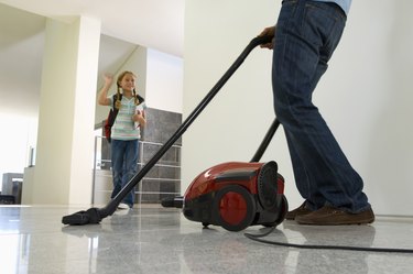 Girl waving at father vacuuming