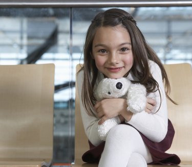 Girl (5-7) sitting in airport hugging soft toy, smiling, portrait