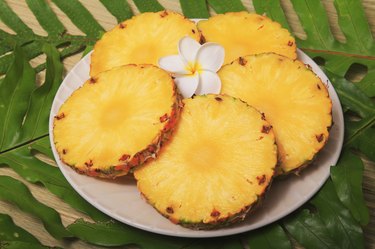 Ripe juicy Pineapple slices on platter with plumeria sitting on green leaves