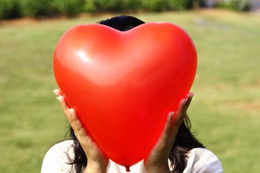 Close-up of a woman holding a heart shaped balloon covering her face