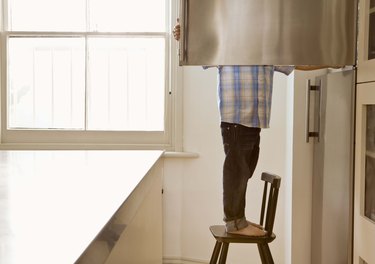 Child standing on chair opening freezer