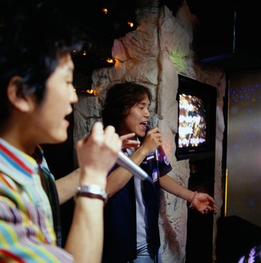 Two young men singing into microphones at karaoke bar