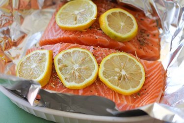 Two salmon fillets on a sheet of foil with seasoning and lemon.