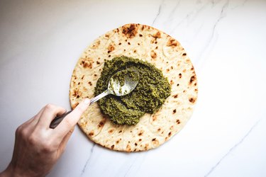 Spreading the pesto sauce of the pizza base.