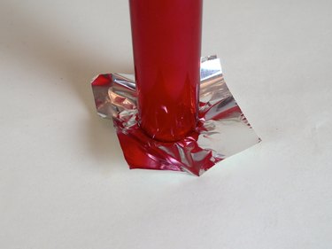 The end of a red tube imprinting a circle onto foil.