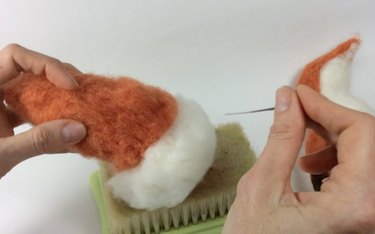 Female hands holding a barbed needle felting needle and orange and white fox tail.