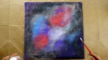Using paintbrush to dot stars on galaxy-themed cushion cover.