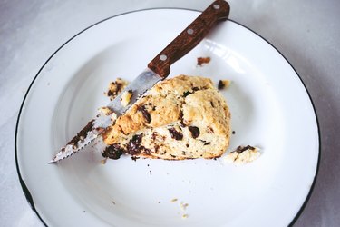 Plate with a knife cutting into a dark chocolate chunk scone.